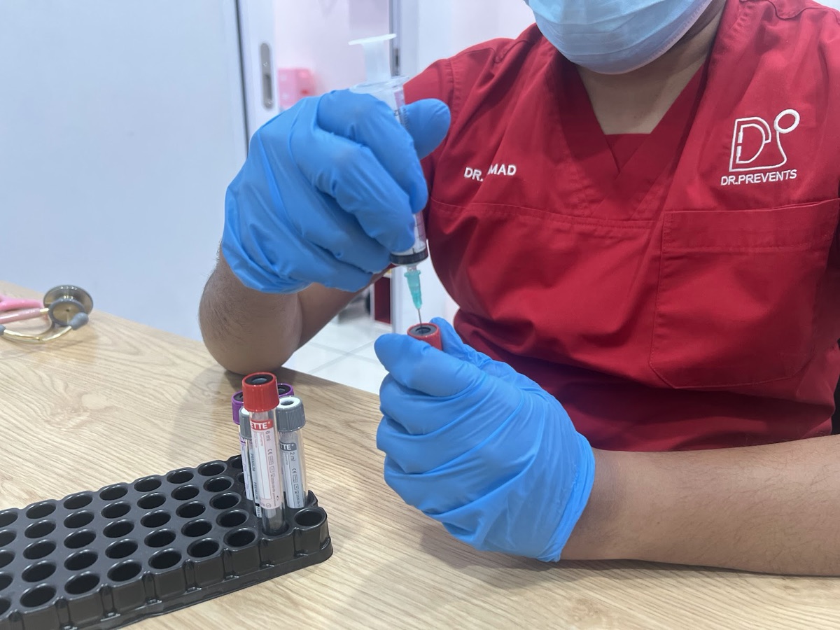 Clinic staff in a red Dr. Prevents uniform preparing blood sample tubes